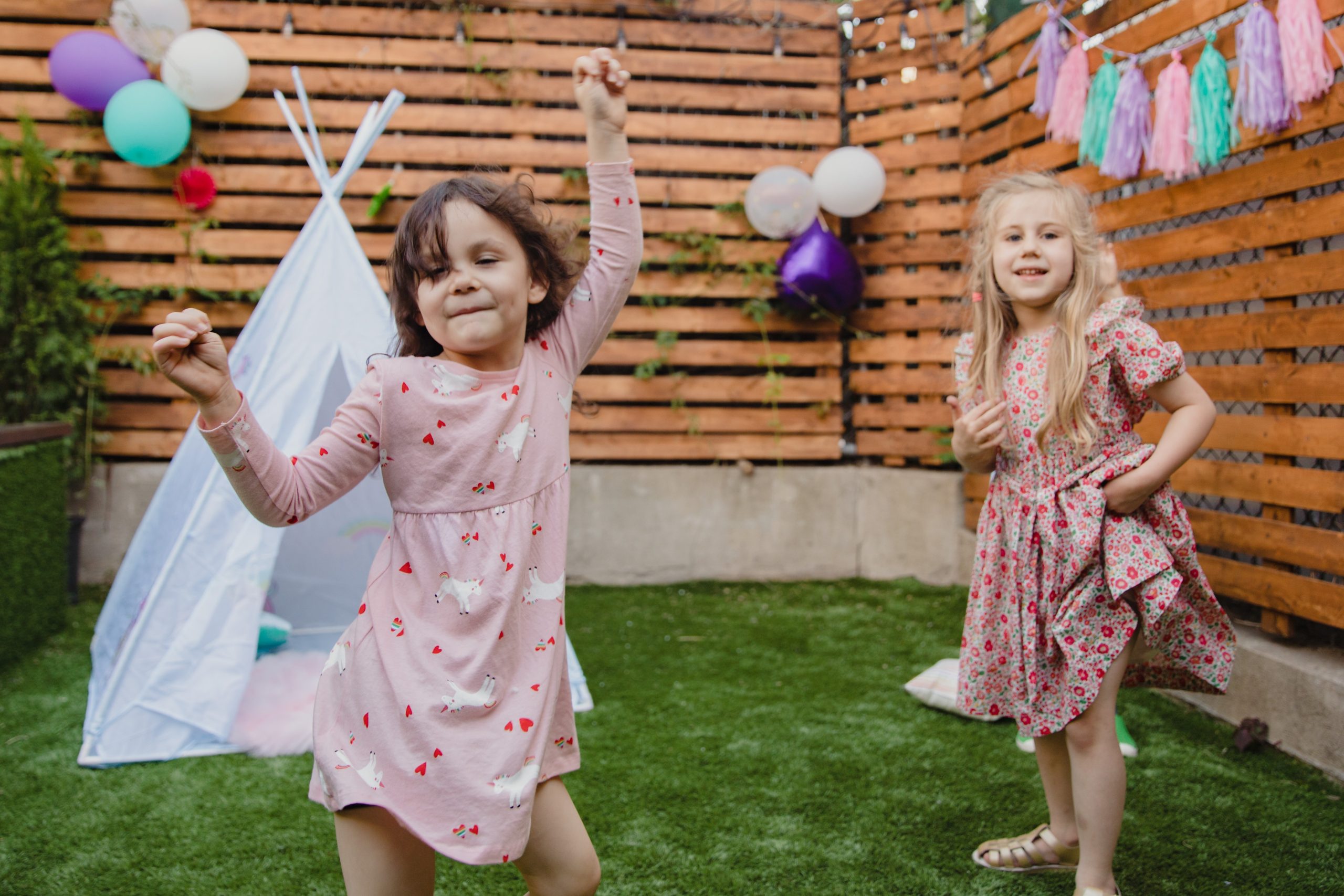 Dans un jardin privé bordé de bois, deux petites filles dansent. Derrière elles, un tipi blanc.
